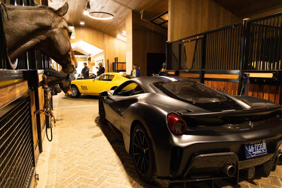 Cars in barn aisle with horses looking out of stalls