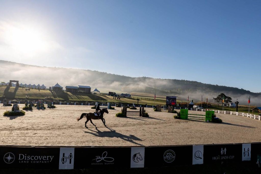 Horse and rider in stadium ring with misty clouds in background.