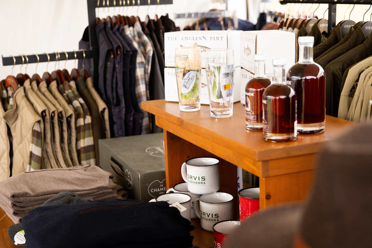Shelf with mugs, glasses, and bottles set between racks of clothing.